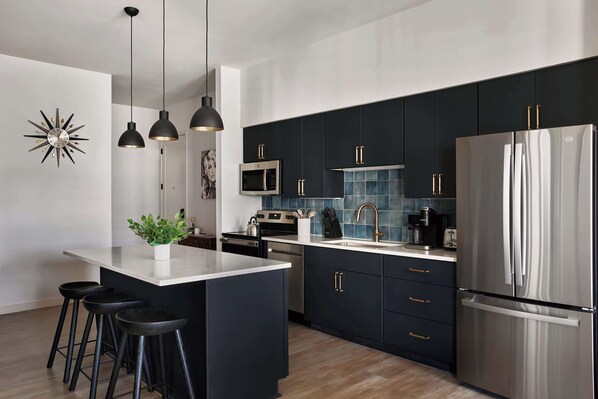 A modern kitchen with dark cabinets, stainless steel appliances, and a central island with stools.