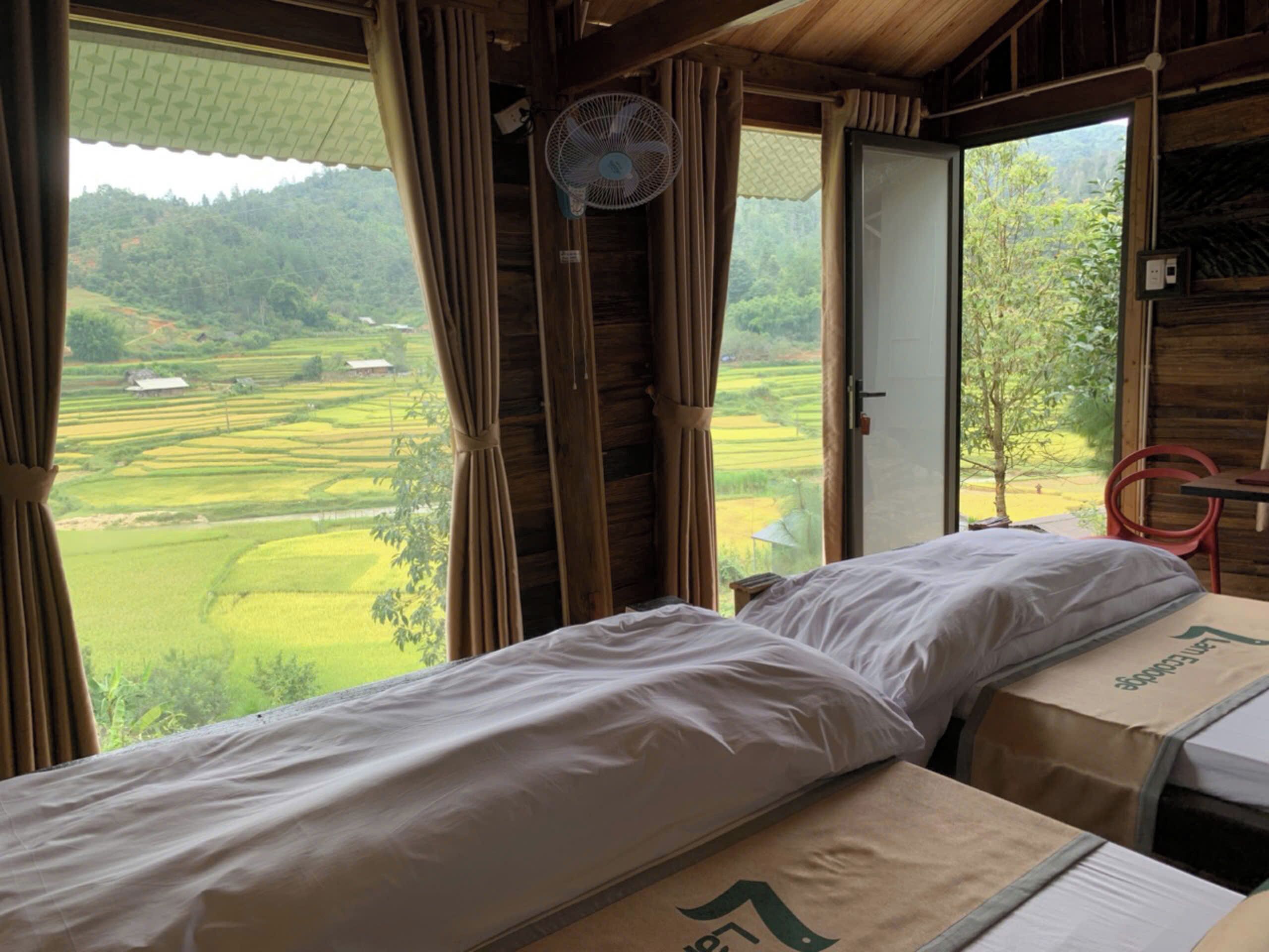 A room with a bed, a fan, and a view of a green landscape.