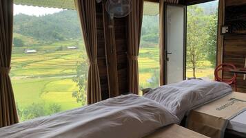 A room with a bed, a fan, and a view of a green landscape.