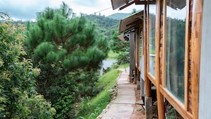 Un edificio de madera con amplios ventanales que dan a un jardín exuberante y una vista distante de una colina.