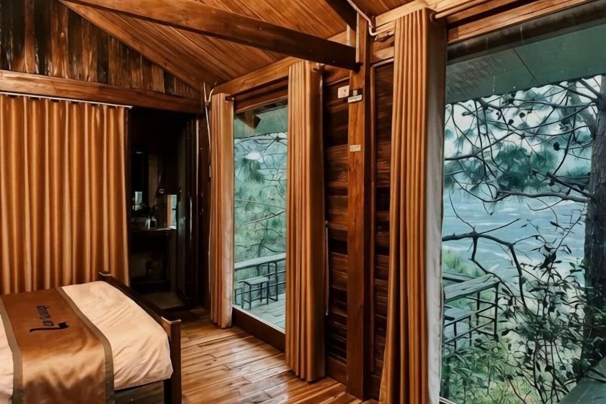 A wooden interior with a bed, a window with curtains, and a view of trees.