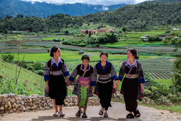 A group of people walking on a path surrounded by terraced fields and mountains in the background.