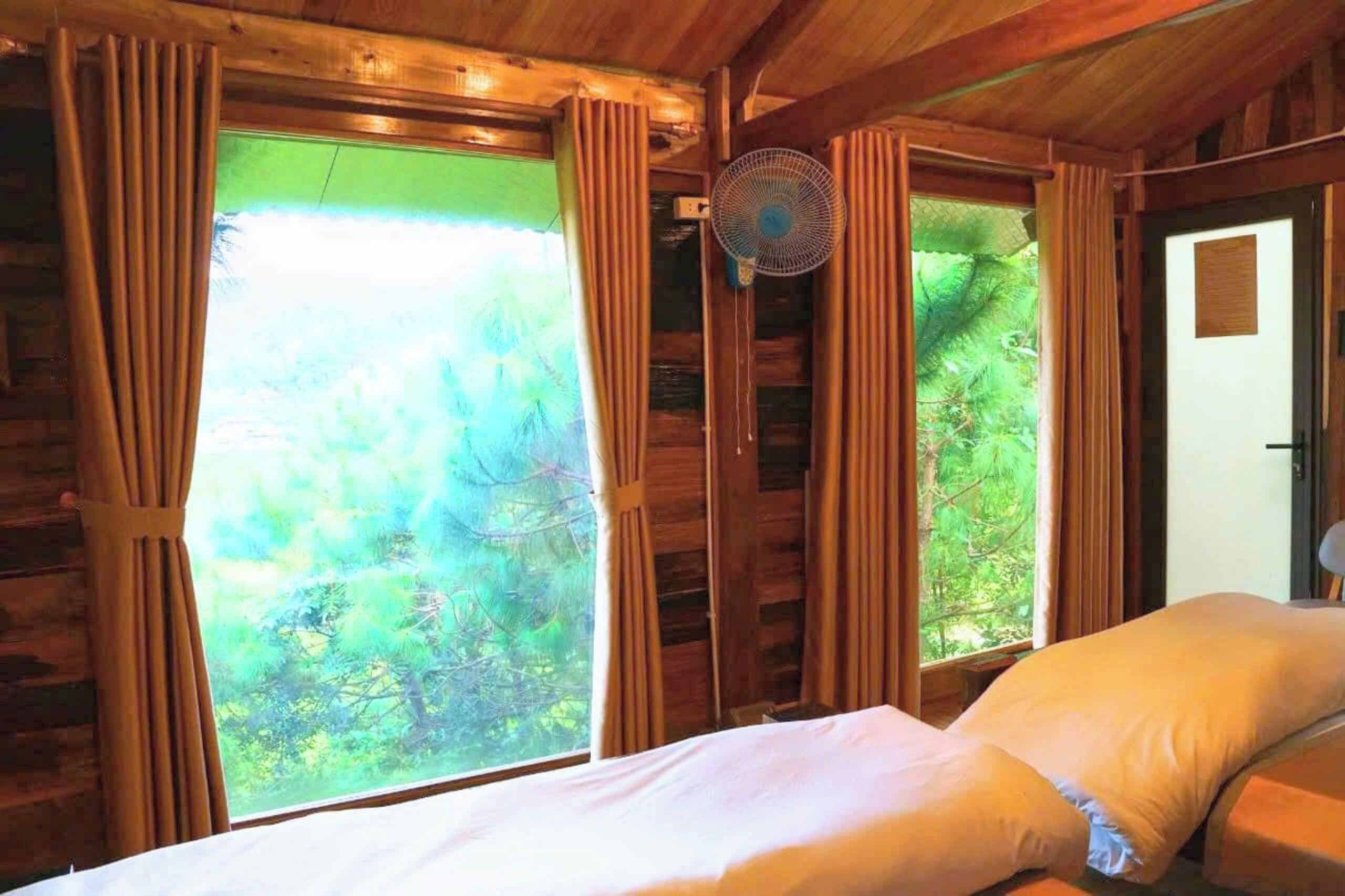 A wooden cabin room with a bed, curtains, and a fan.