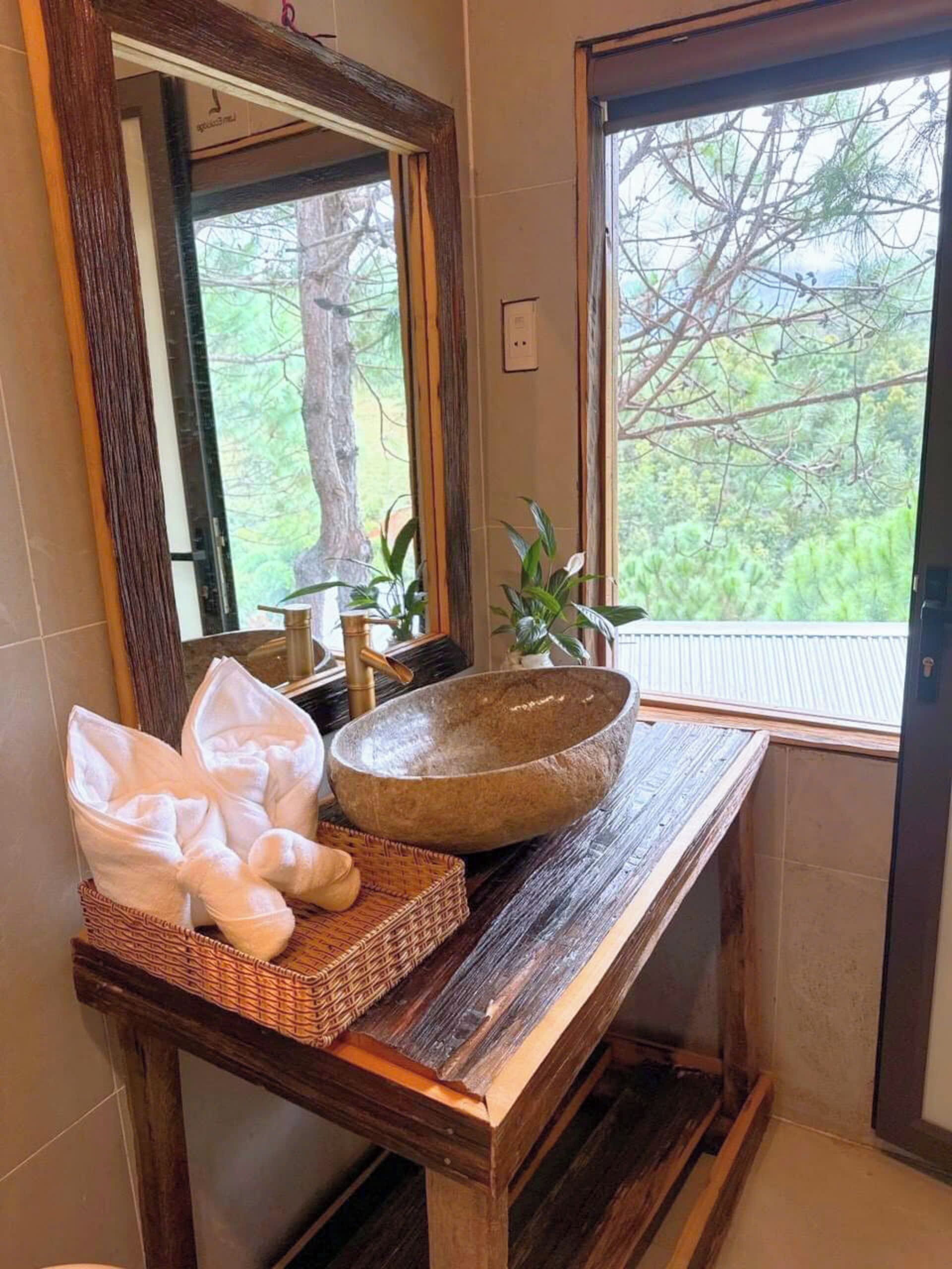 Een badkamer met een houten wastafelmeubel, een ruime stenen wasbak, handdoeken en uitzicht op groen door het raam.
