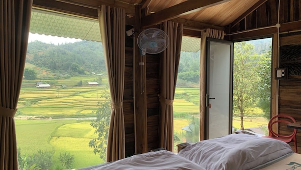 Una habitación de madera con cama, ventilador y vista a un paisaje verde.