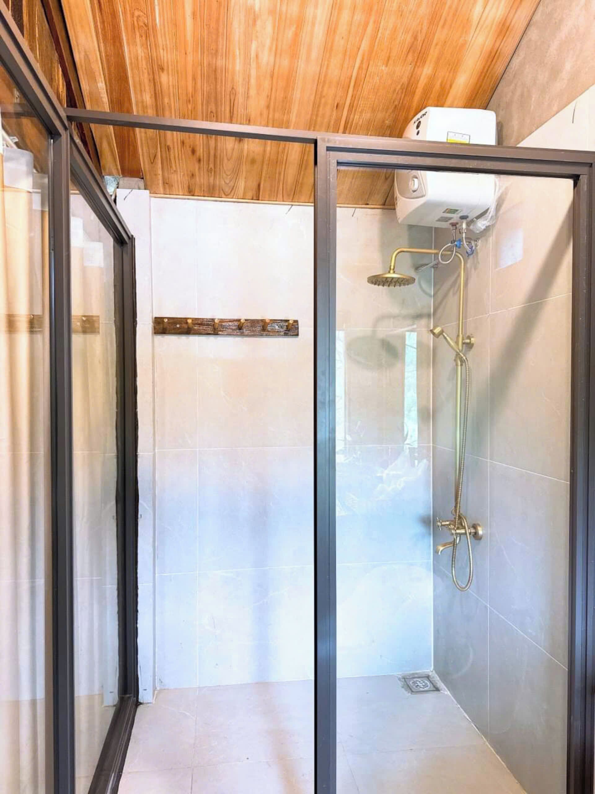 A glass-enclosed shower area with a wooden ceiling, white tiled walls, and a visible water heater.
