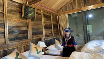 A wooden room with a bed, pillows, a fan, and a person standing by the bed.