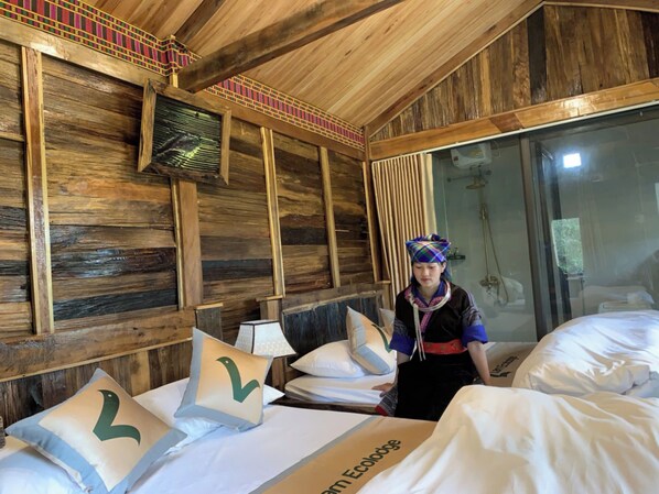 A wooden room with a bed, pillows, a fan, and a person standing by the bed.