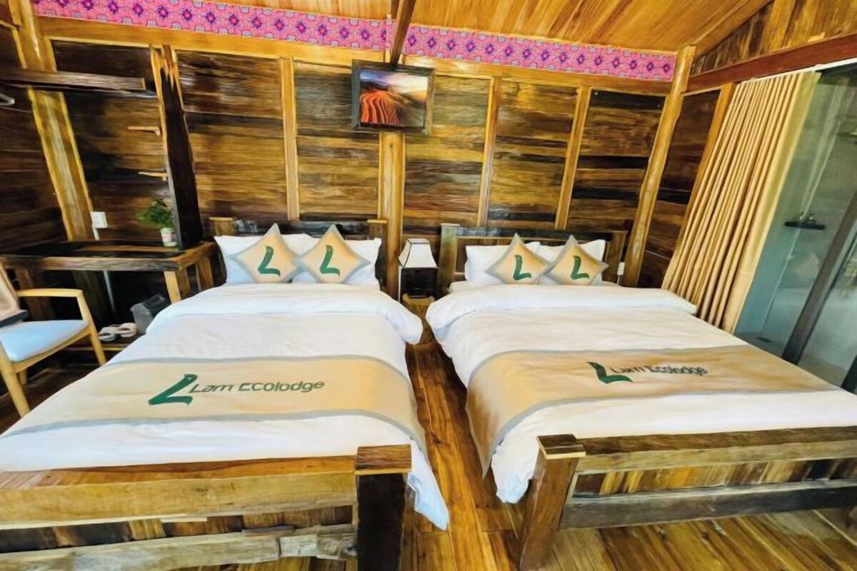 A room with two beds, each with a headboard and pillows, and a small table with a chair.