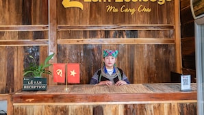 Un mostrador de recepción con fondo de madera, un cartel que dice "Lam Ecolodge Mu Cang Chai" y una bandera con una estrella amarilla.