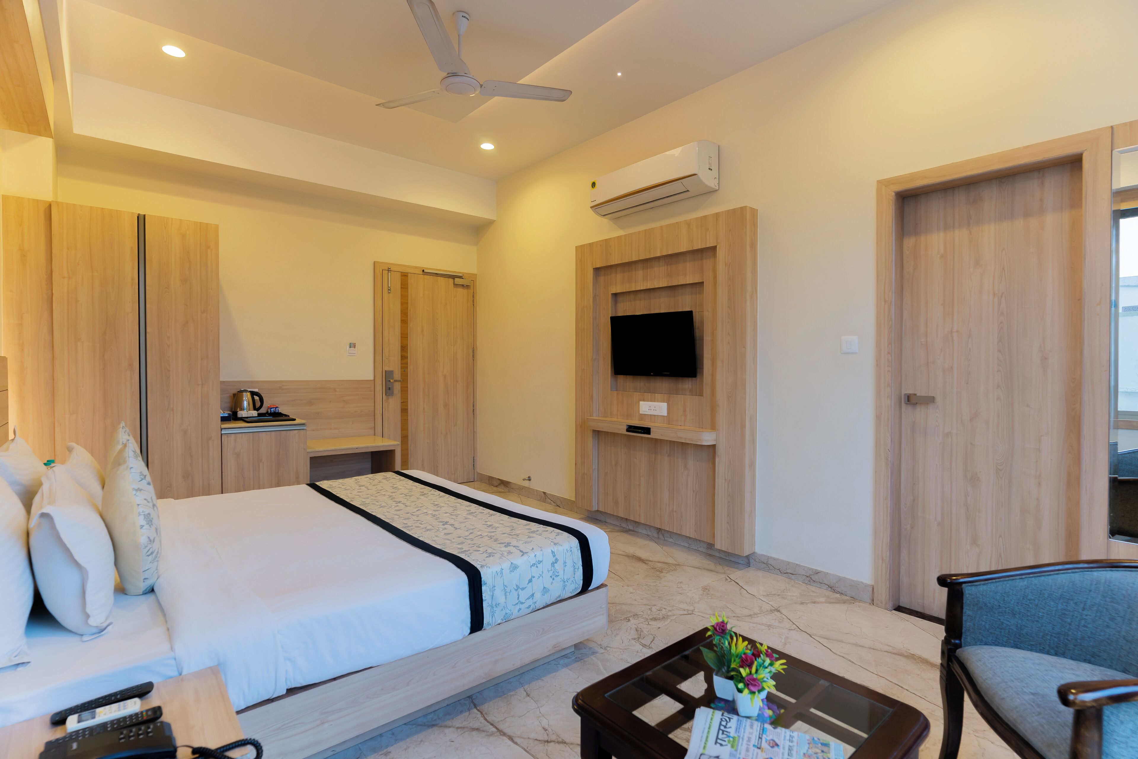 Habitación de hotel con cama, escritorio, silla, mesa de centro, aire acondicionado, televisor y ventilador de techo.