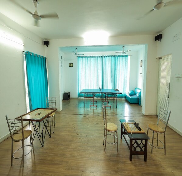 A spacious room with a wooden floor, a table with chairs, a sofa, and a chess table. - Kovalam Studio Villa (Tirupporur)
