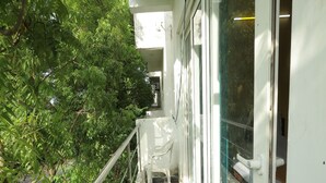 A balcony with a white chair, a potted plant, and a glass door. - Kovalam Studio Villa (Tirupporur)