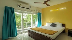 A bedroom with a bed, curtains, an air conditioning unit, a ceiling fan, and a view through a window. - Kovalam Studio Villa (Tirupporur)