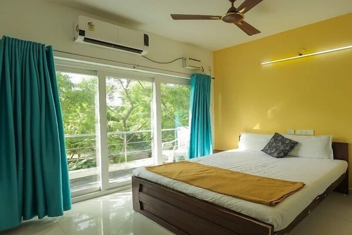A bedroom with a bed, curtains, an air conditioning unit, a ceiling fan, and a view through a window.