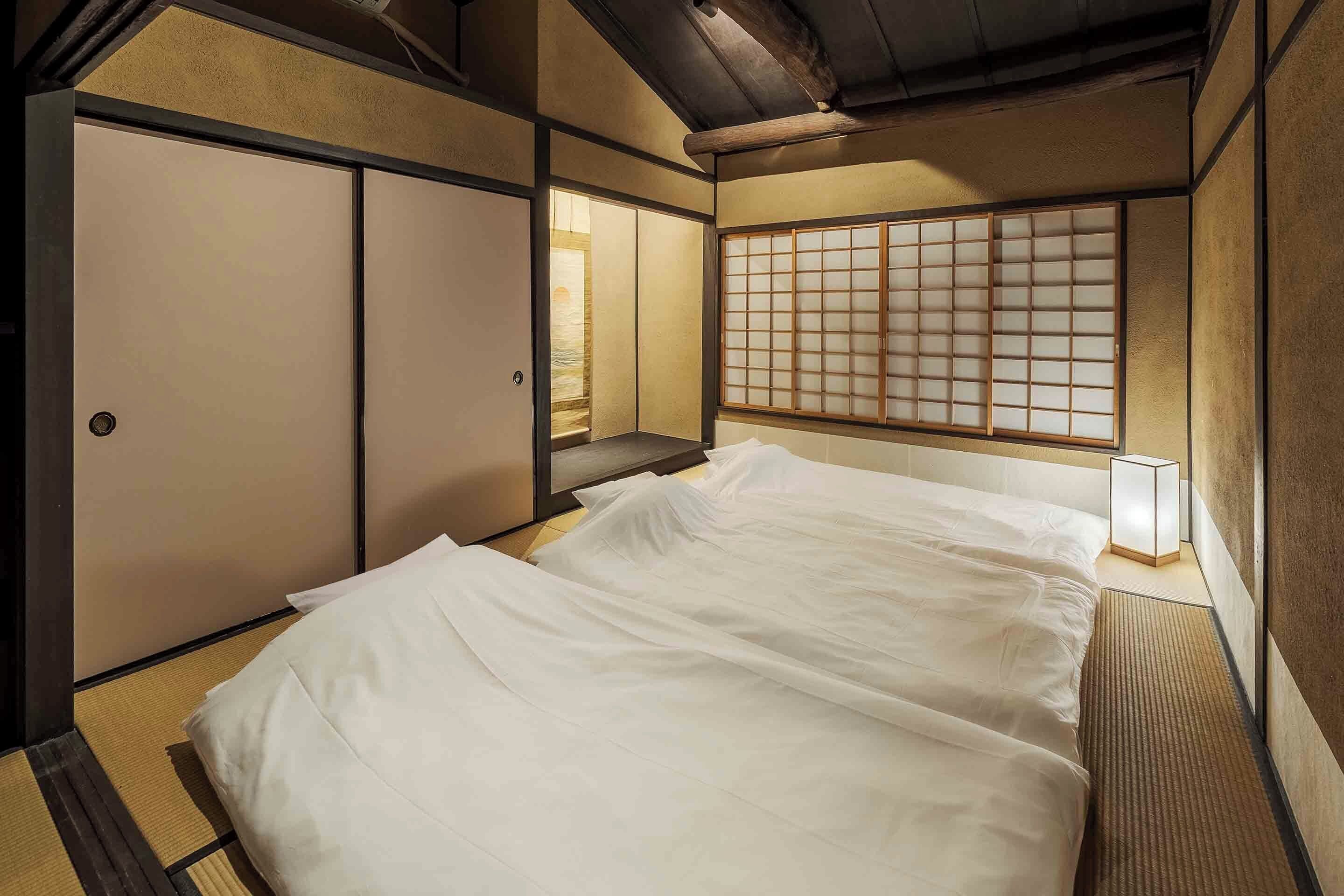 A traditional Japanese-style room with tatami flooring, a low bed with white bedding, sliding doors, and a shoji screen.