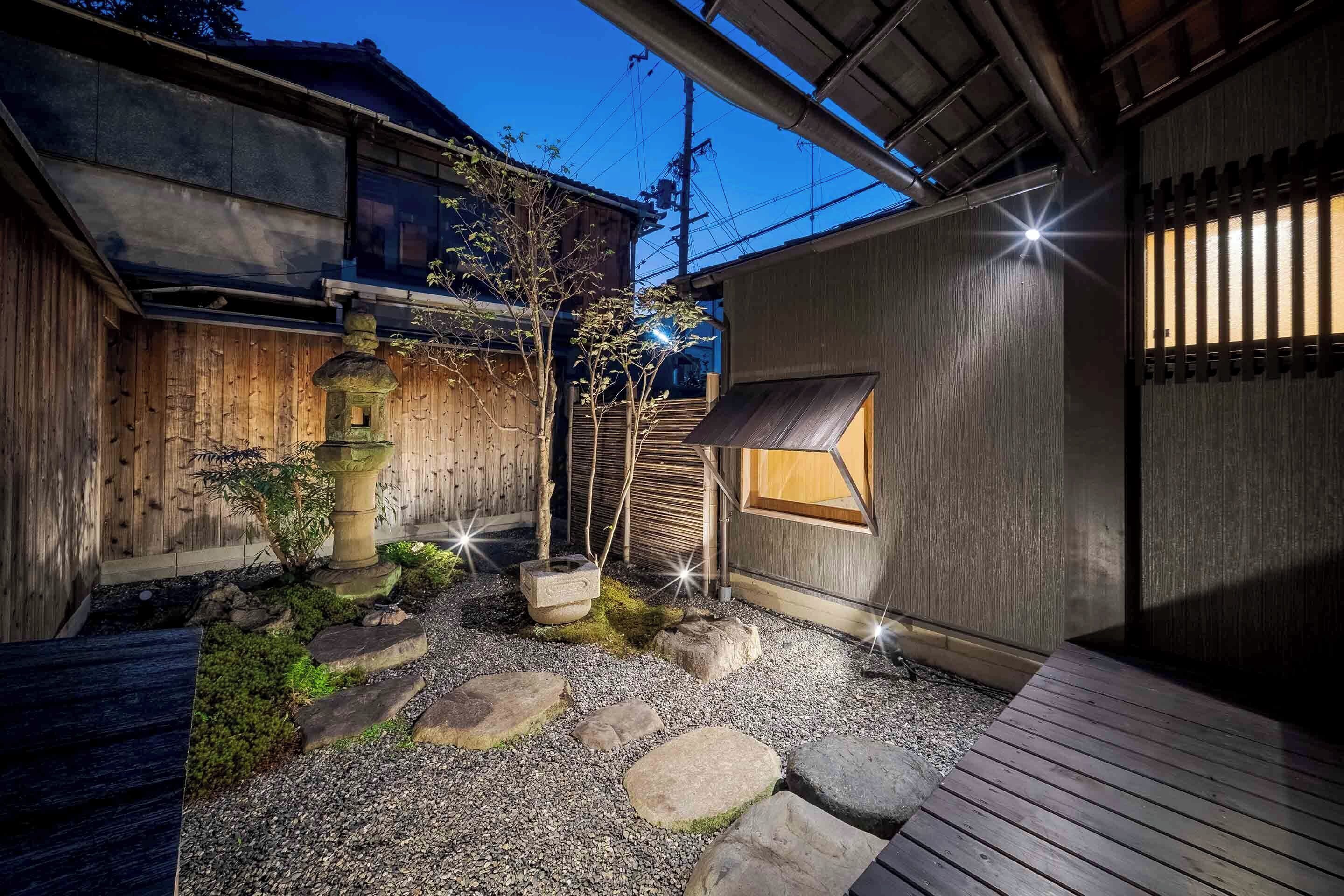 A traditional Japanese garden with a wooden structure, stone steps, and a small window.