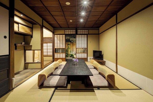 A traditional Japanese room with tatami flooring, a low table, cushioned seating, and a television. - Yura Machiya Holiday House (Kyoto)
