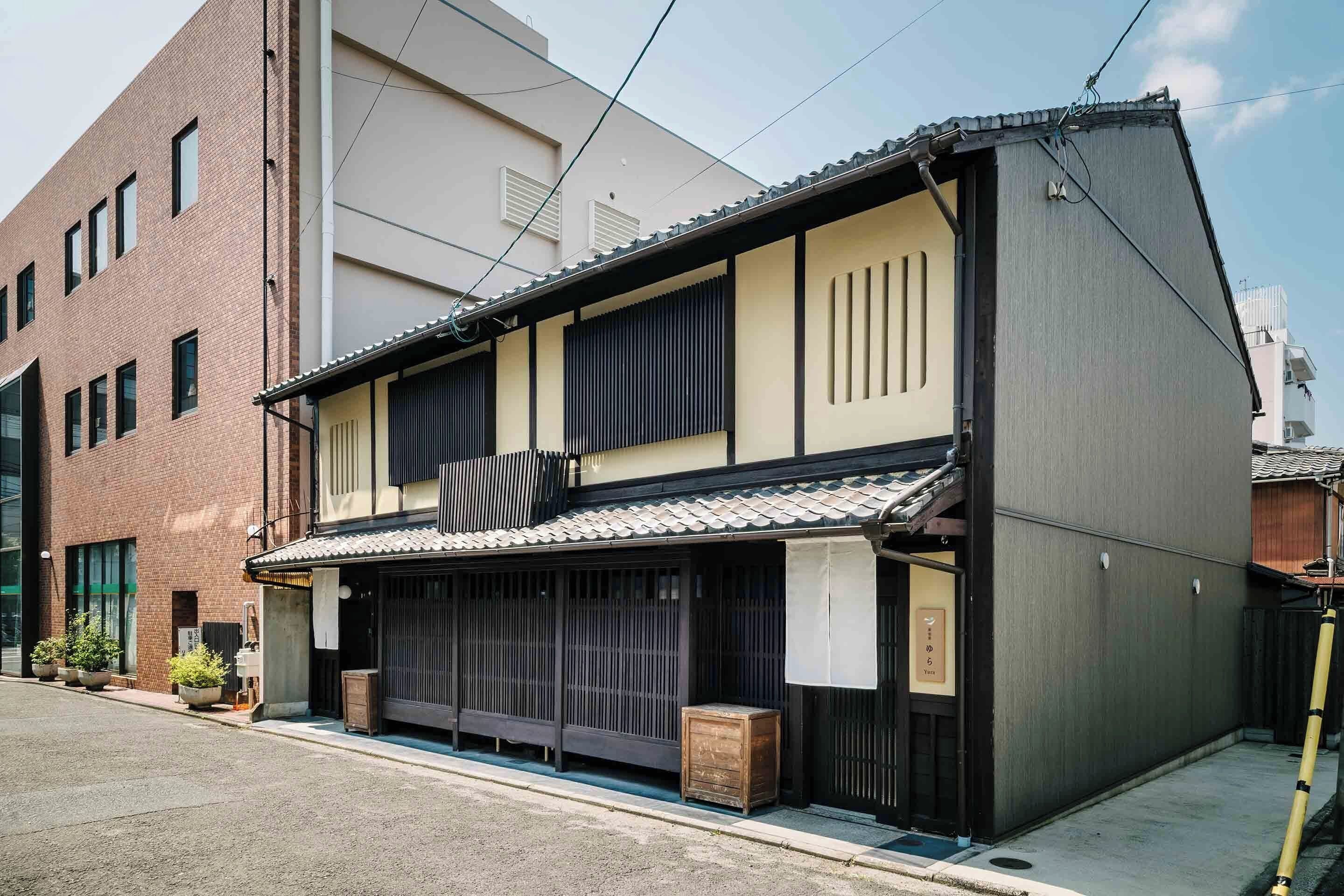 Een traditioneel Japans gebouw met pannendak, houten schuifdeuren en een klein houten bijgebouw ervoor.