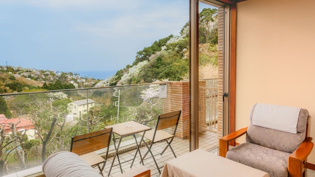 Un balcone con tavolo e sedie, affacciato su una collina con edifici e alberi.