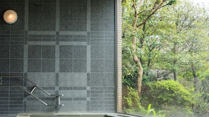 Un'area benessere con parete rivestita in piastrelle, piscina vetrata e vista sul verde.