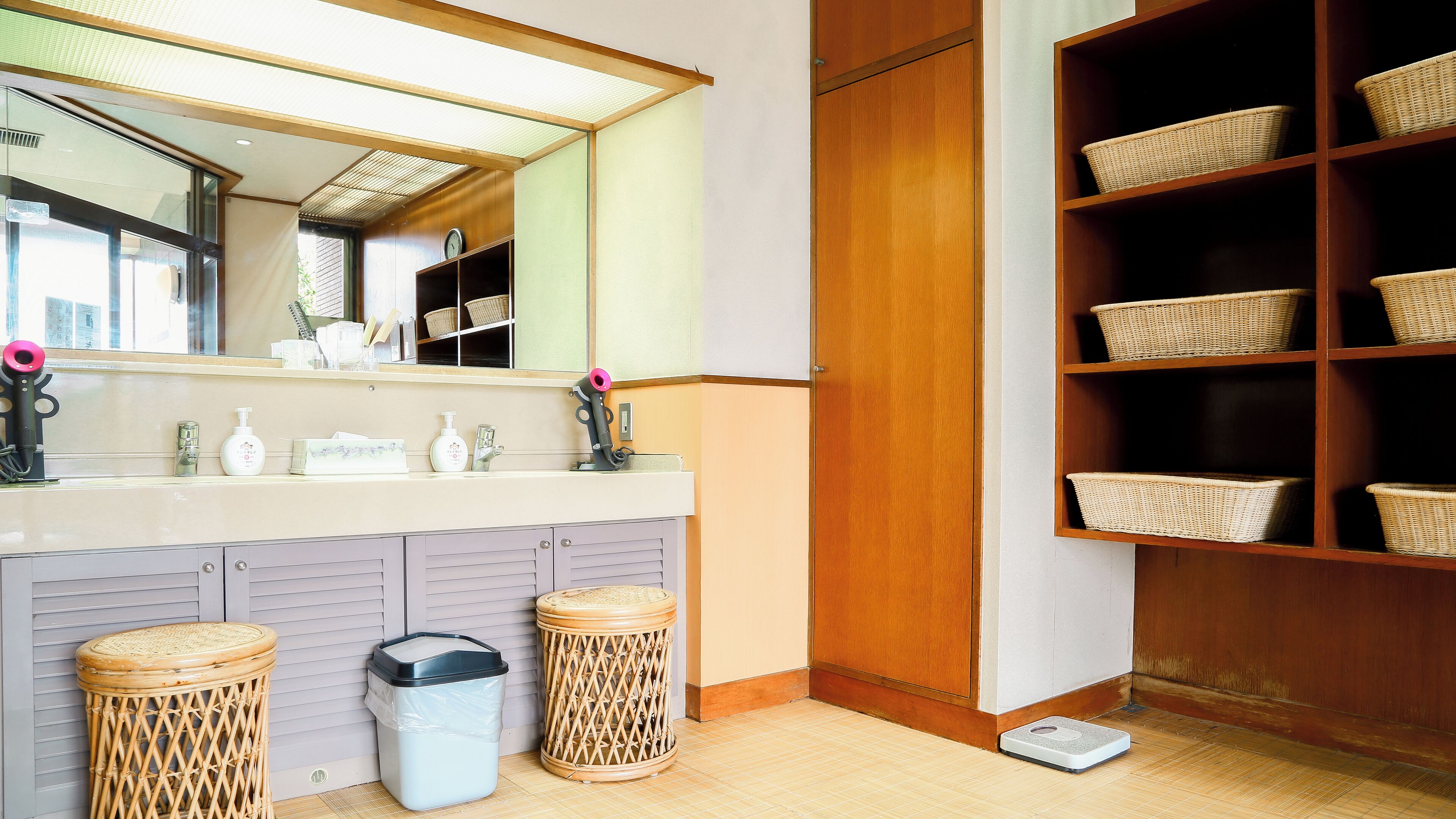 A bathroom with a large mirror, a sink, and a shelf with baskets.