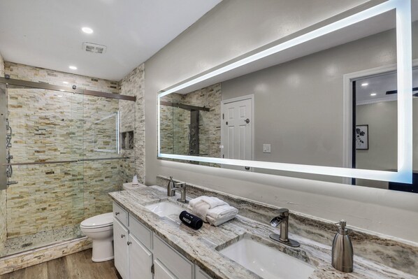 Un baño moderno con cabina de ducha de vidrio, un espejo grande y encimera de mármol.