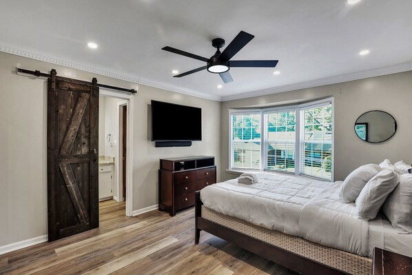 A bedroom with a bed, a ceiling fan, a TV, a dresser, and a window with blinds.