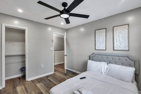 A bedroom with a bed, a ceiling fan, a wardrobe, and a door leading to another room.