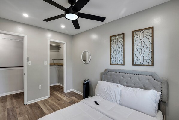 A bedroom with a bed, a ceiling fan, a mirror, and decorative wall panels.