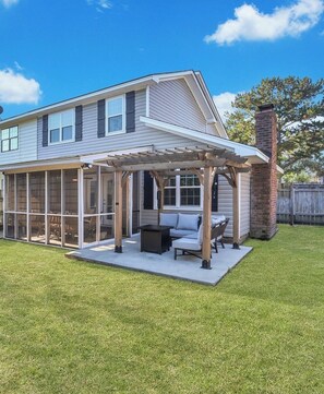 Relax on the covered patio with a sofa and dining table, surrounded by a lawn and secure fence.