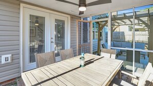 Un patio techado con una mesa y sillas de madera, un ventilador de techo y un gran ventanal corredizo.