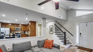 Una sala de estar moderna con un sofá modular gris, una escalera y una cocina visible a través de una puerta abierta.