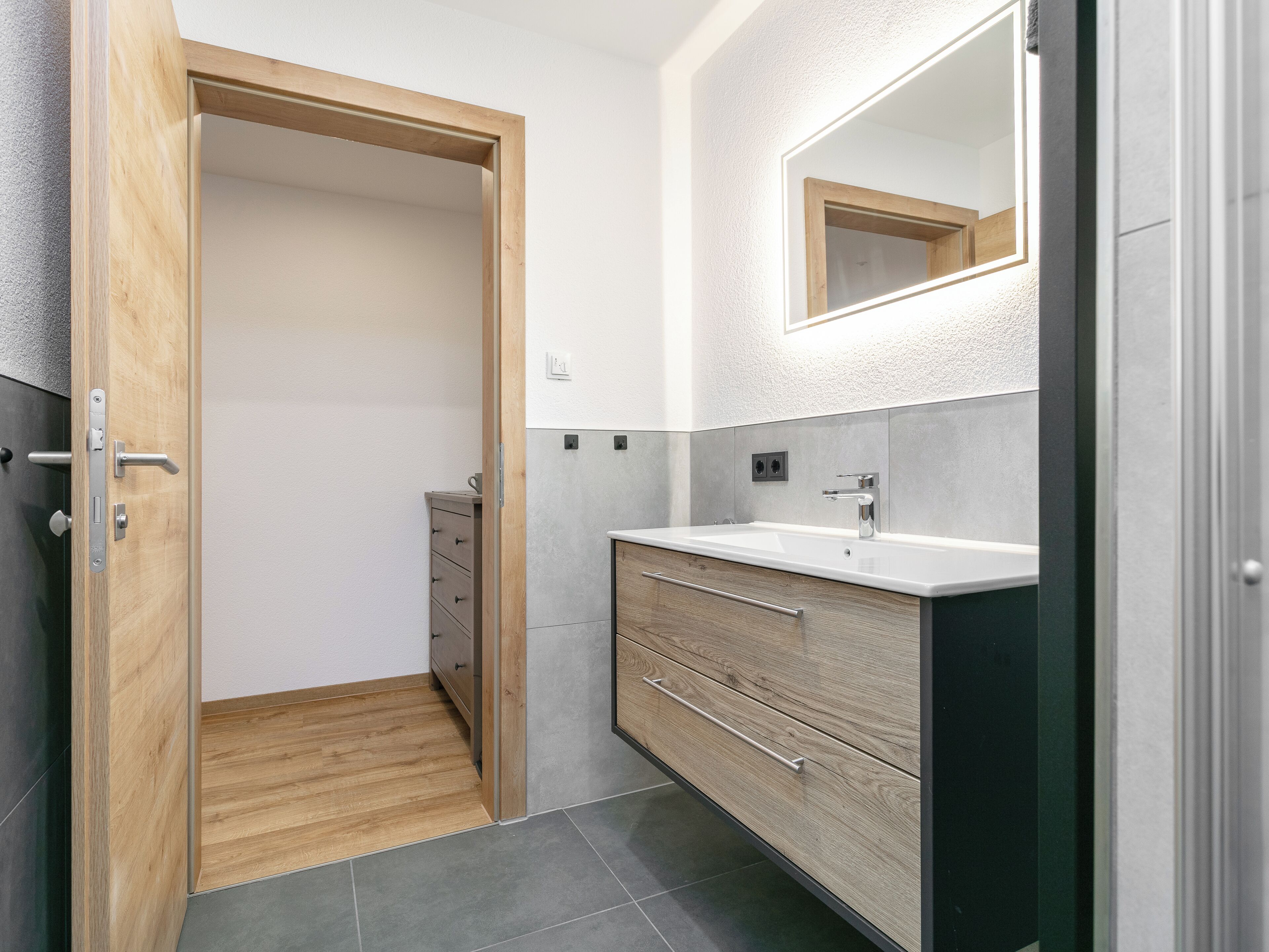 Ein modernes Badezimmer mit einer Holztür, einem weißen Waschbecken und einem Spiegel darüber.