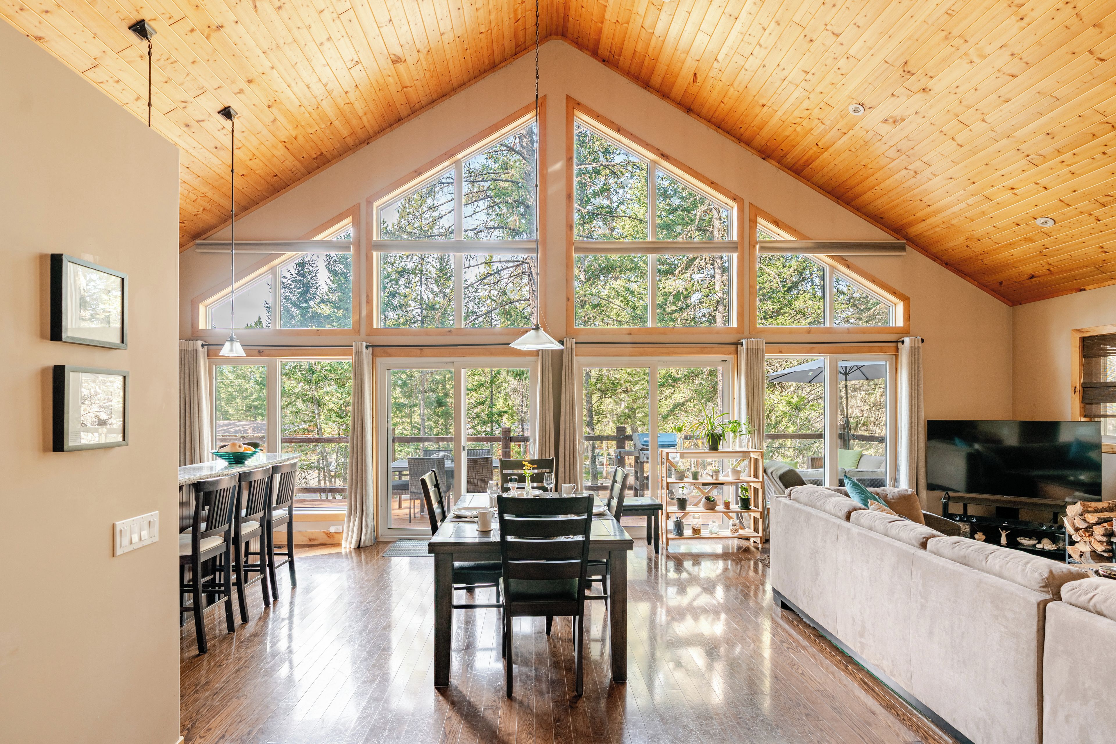 A spacious interior with a high ceiling and large windows, a dining area, and a seating area with a television.