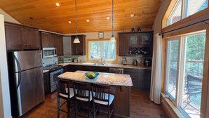 Una cocina con armarios de madera, un refrigerador de acero inoxidable, un microondas, una estufa, un lavamanos y un ventanal grande.