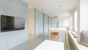 A modern living room with a flat-screen TV mounted on the wall, a dining table with chairs, and a built-in bench with cushions. - HOTEL ReONcE Shibuya (Tokyo)