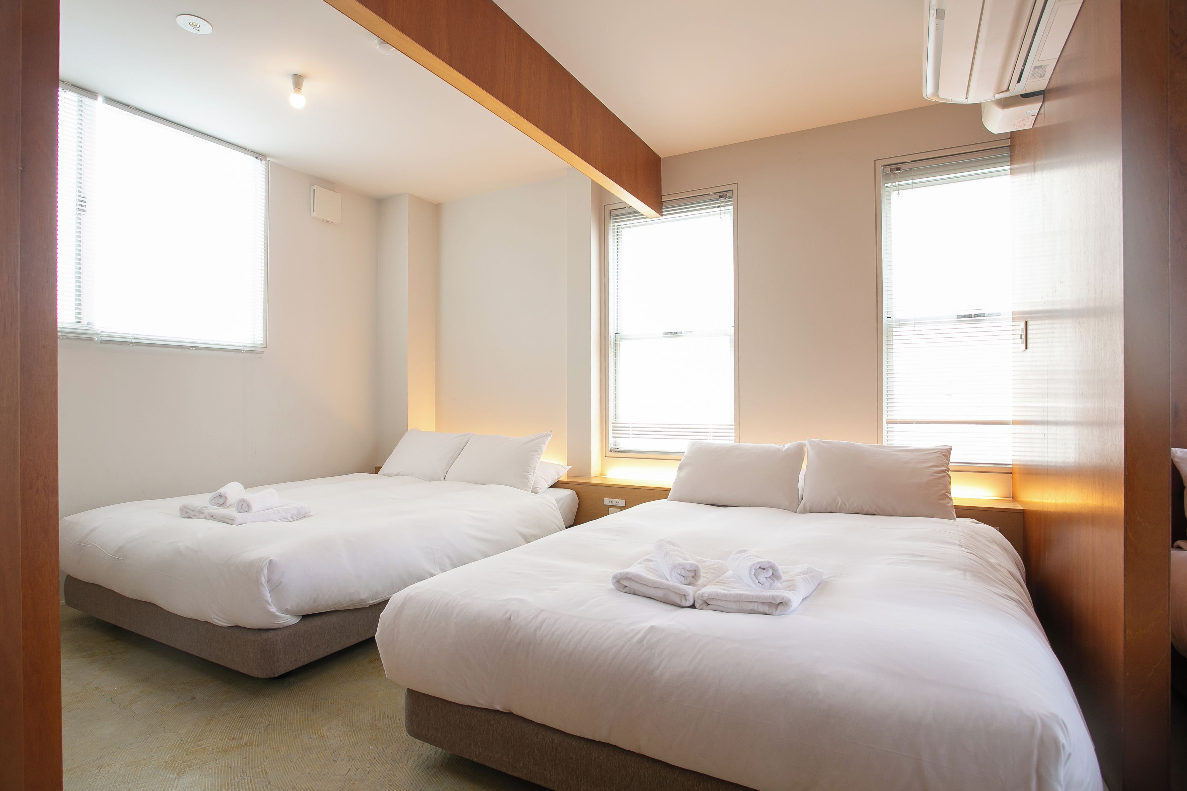 Een hotelkamer met twee bedden, elk voorzien van witte lakens en handdoeken, een houten plafond en grote ramen met zonwering.