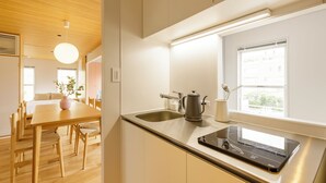 A modern kitchen with a wooden dining table, chairs, a sink, a kettle, and a window with a view. - HOTEL ReONcE Shibuya (Tokyo)