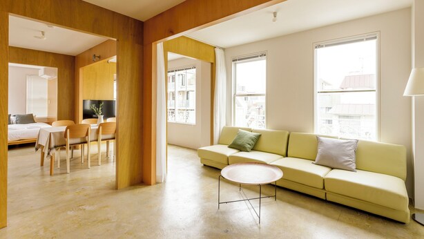 A modern living room with a sofa, dining table, and chairs. There is a bed in the background, a TV on a stand, and large windows providing natural light. - HOTEL ReONcE Shibuya (Tokyo)