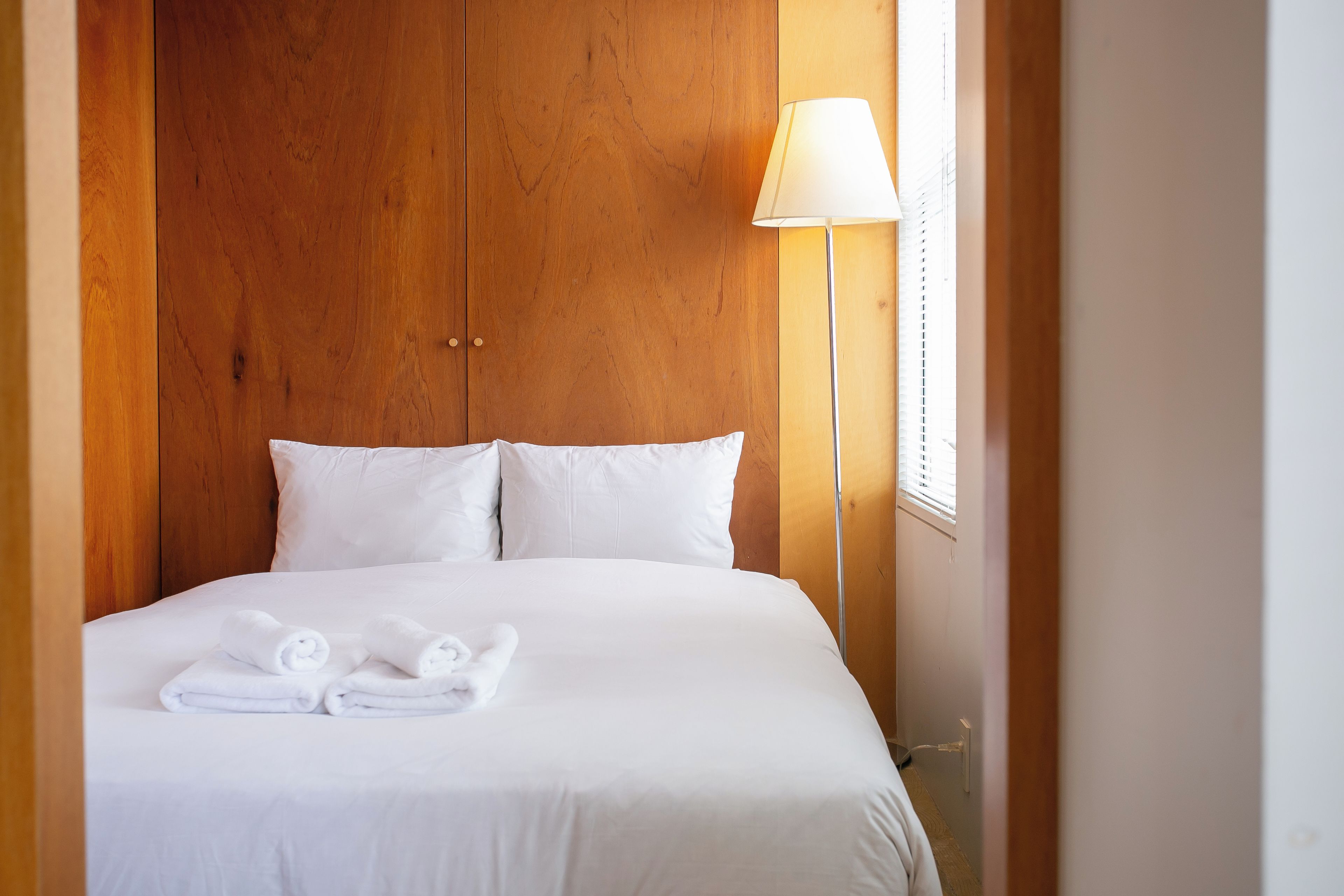 Une chambre d’hôtel avec un lit, des oreillers, une lampe et une fenêtre.