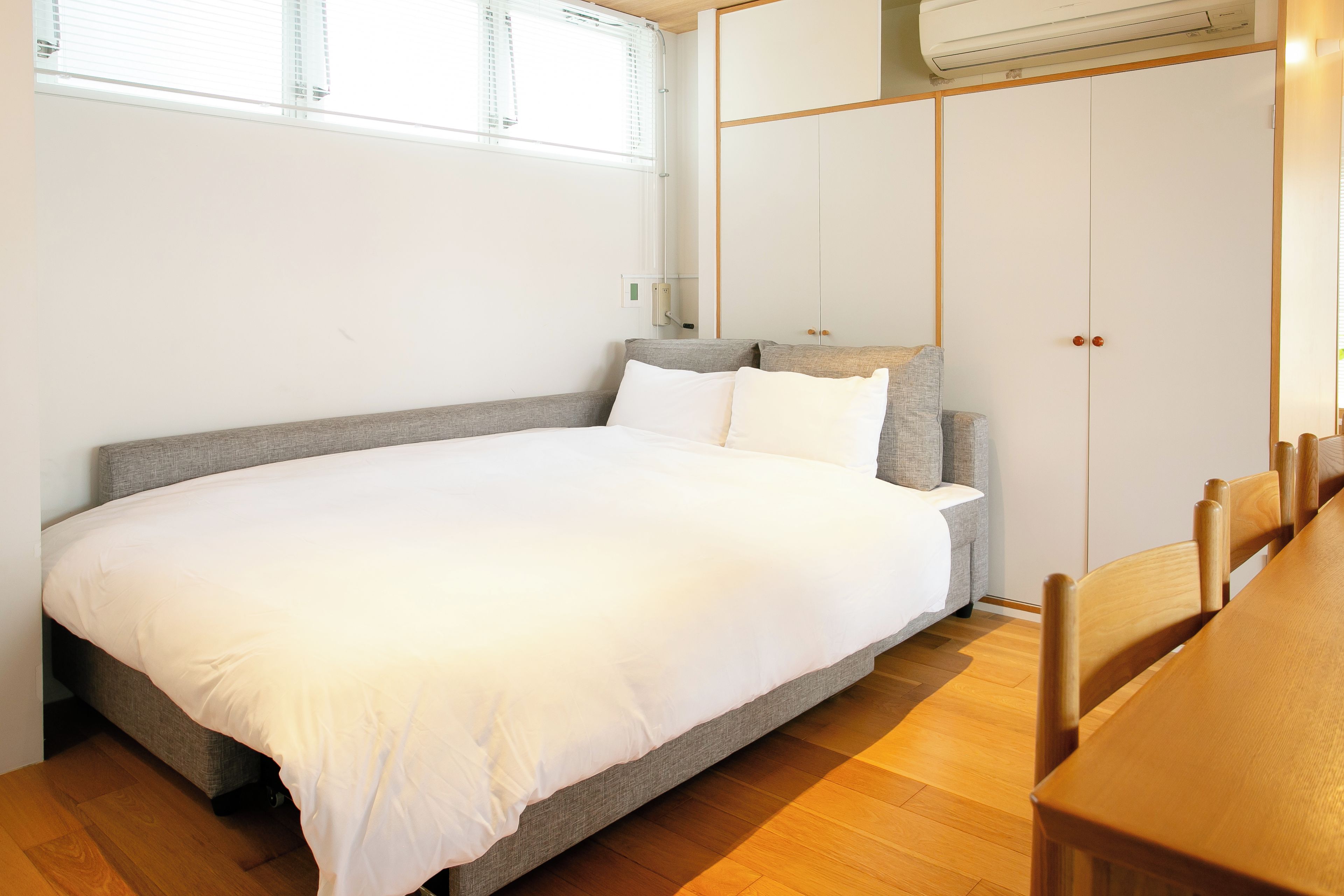 Un dormitorio con cama, armario, ventana y aire acondicionado.