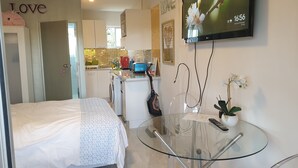 A modern hotel room with a bed, a glass table, a TV, and a kitchenette in the background. - CUTE, COMFY, AFFORDABLE STUDIO 23 +CARPARK  (Auckland)