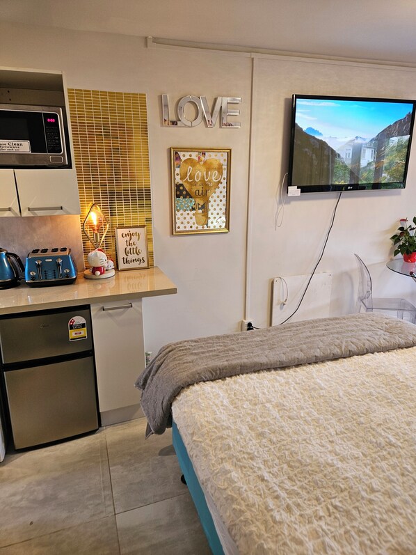A modern bedroom with a bed, a TV, a microwave, a toaster, and a small fridge.
