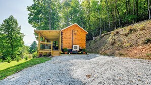 Eine Holzhütte mit Veranda, umgeben von einem Schotterweg und bewaldetem Hang.