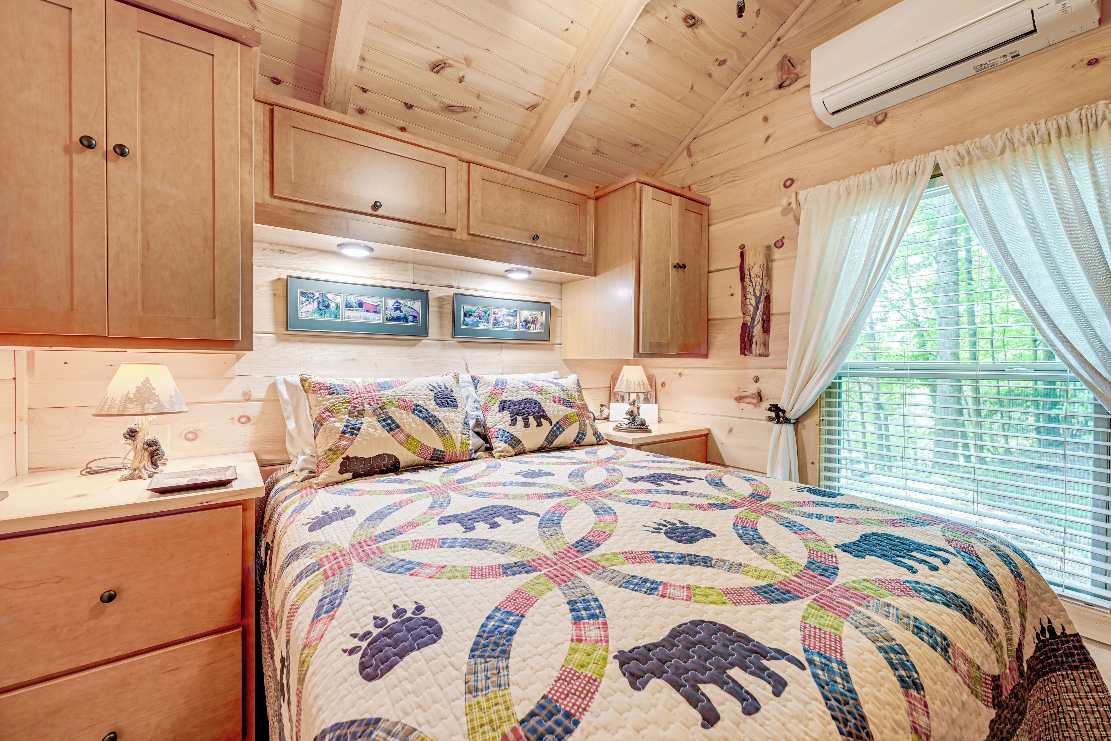 Een slaapkamer in een houten chalet met een gewatteerde spreideken, houten kasten, een nachtkastje en een raam met gordijnen.