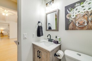 A bathroom with a wooden cabinet, a white sink, a mirror, and a toilet. - Home w/ Trail Access & Fire Pit in Bella Vista! (Bella Vista)
