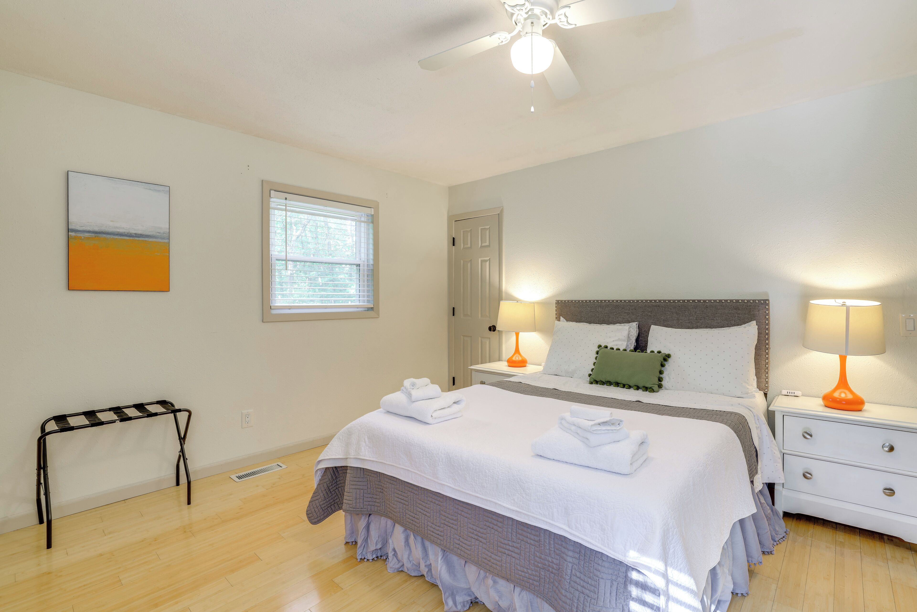 A neatly arranged bedroom with a bed, bedside lamps, a standing lamp, a ceiling fan, and a window with blinds.
