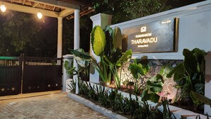 En hotellentrén med en skylt som visar texten ”Kumarakom Tharavadu Sarabhog Hotel” och en traditionell träport.