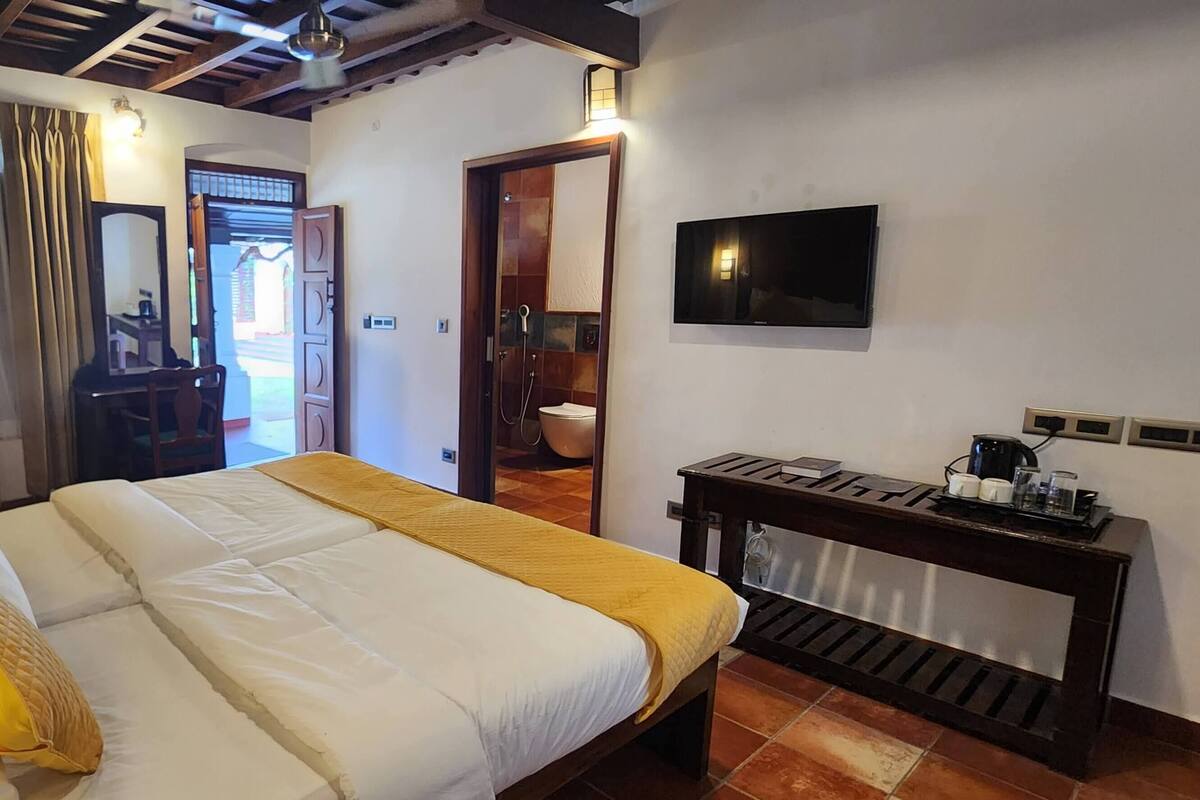 Habitación de hotel con cama, escritorio con cafetera, televisor y zona de ducha.